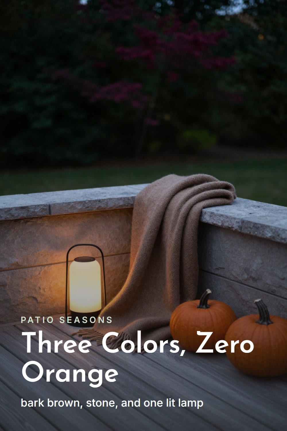 A quiet patio corner with one lit lamp, a bark-brown wool throw, and a stone-colored planter