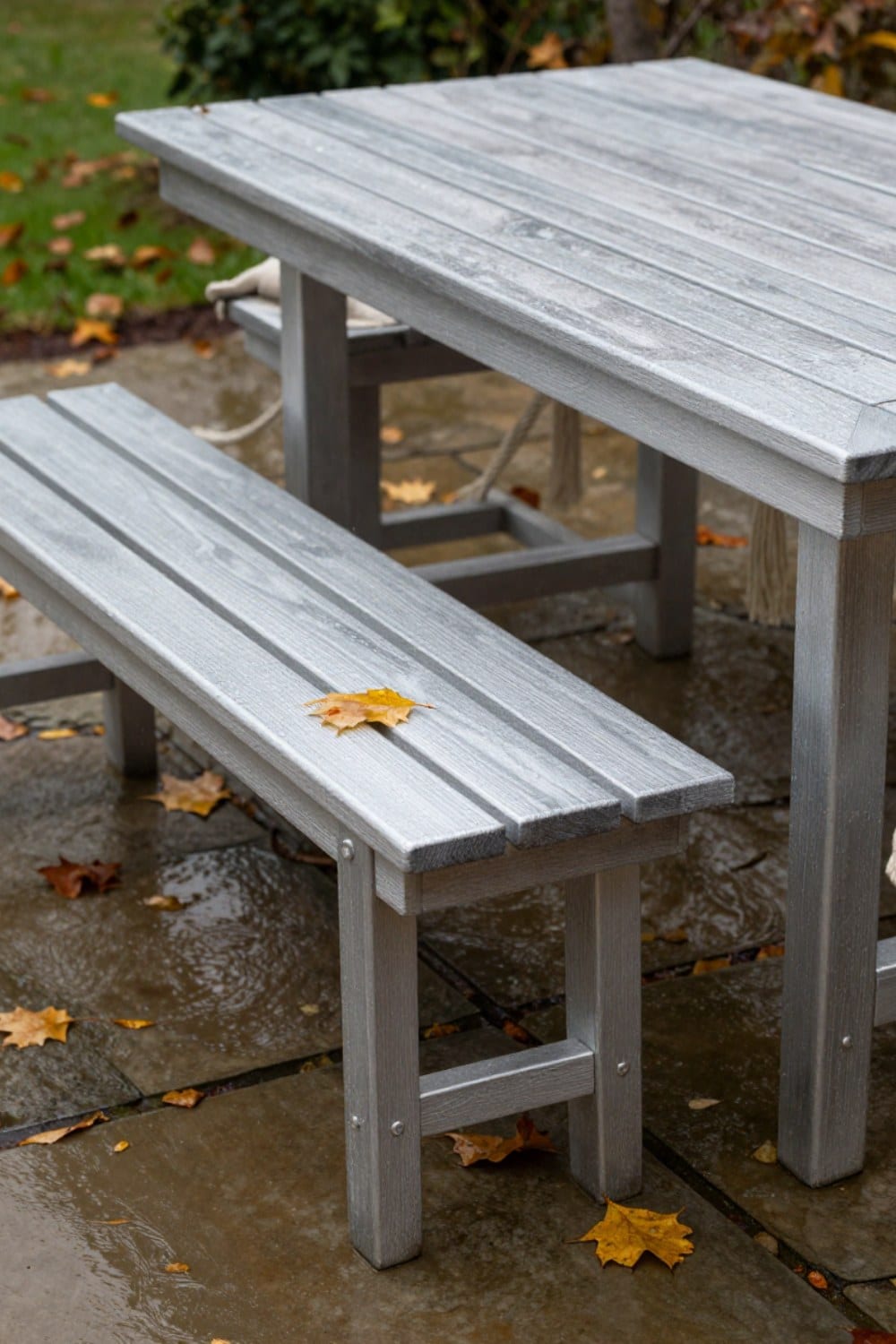 A fall patio scene with rain beading on silvered teak and wet leaves scattered across the stone