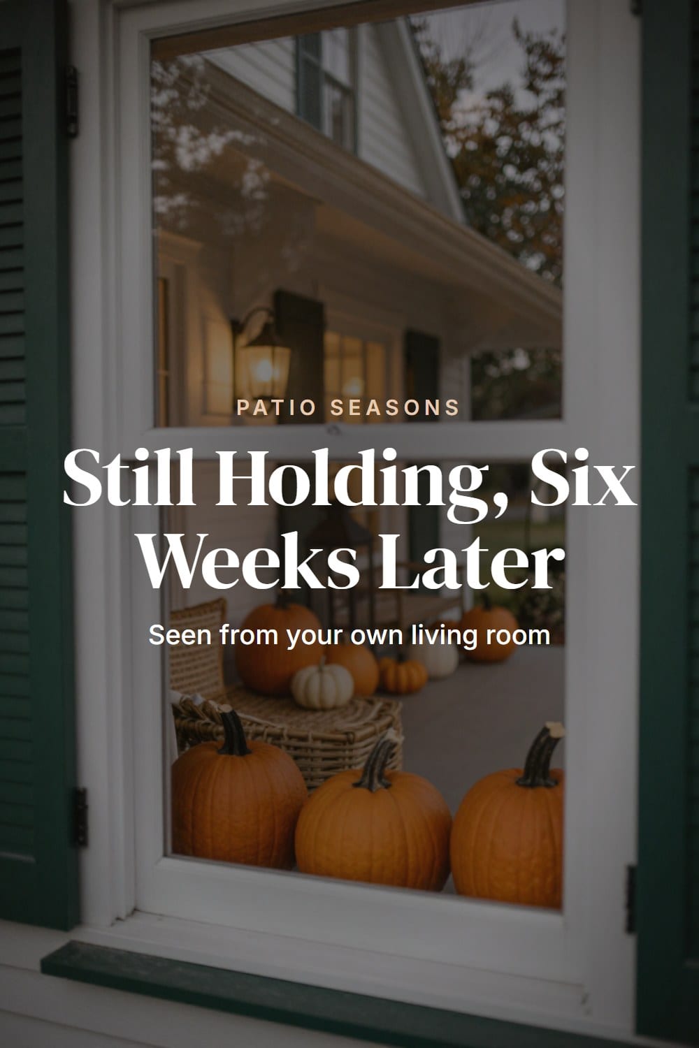 View from inside the house through a window at a lit lantern and pumpkins on the styled front porch