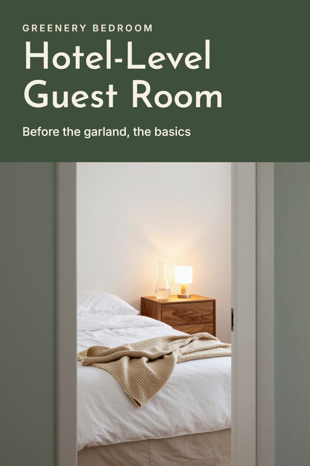 A guest bed made up in crisp white percale with a folded oatmeal blanket and a carafe on the nightstand under a warm lamp
