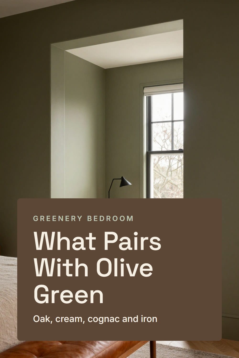 Doorway view of an olive green bedroom with a cognac leather bench, oatmeal linen bed and black iron lamp beside an oak nightstand