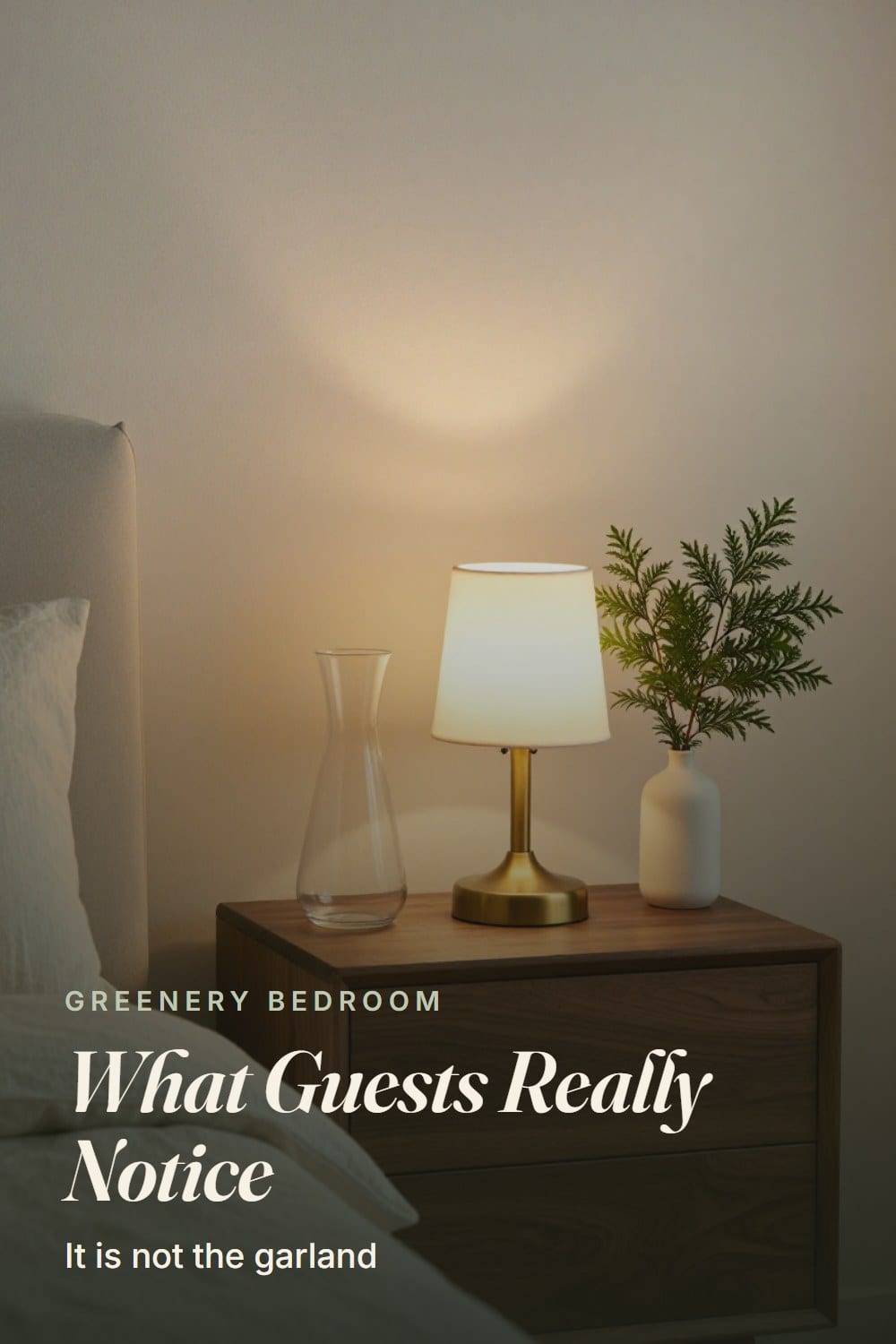 A walnut nightstand with a glass carafe, a brass lamp and a sprig of cedar in a small white vase